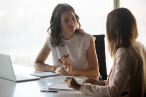 Two women in an office meeting room talking to each other.