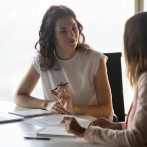 Two women in an office meeting room talking to each other.