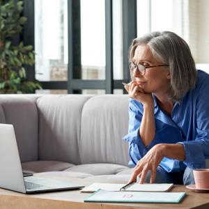 Businesswoman reviewing paperwork and computer screen while sat on a sofa