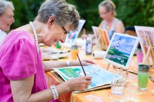 Group of care home residents smiling and painting outdoors.