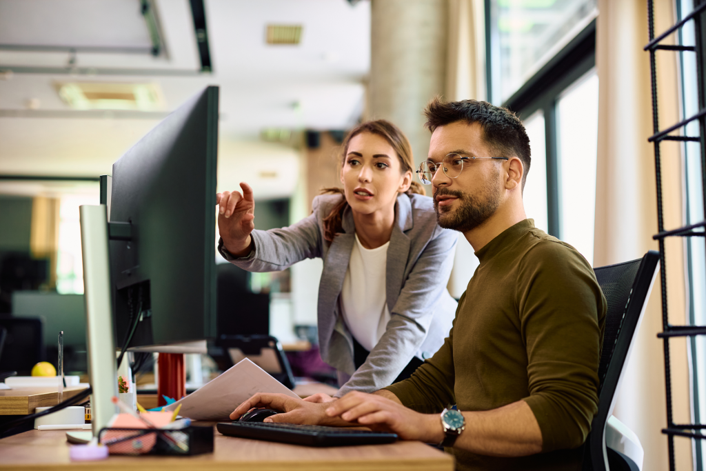 Female teachers shows man how to complete a task on a computer