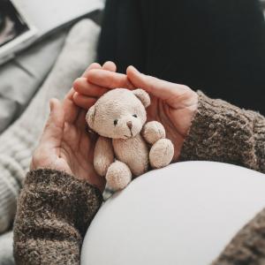 Woman pregnant belly with little teddy toy bear.