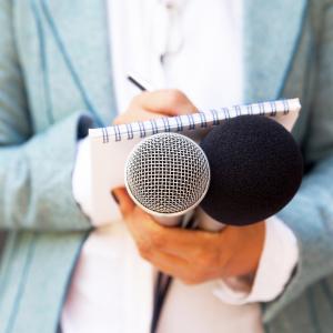 Female reporter at press conference, writing notes, holding microphone