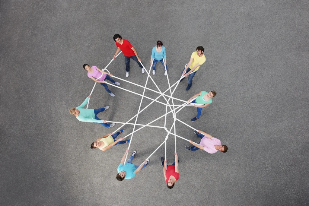 Photograph from above of a group of people all connected in a circle with a log piece of rope