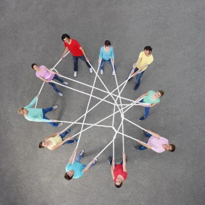 Photograph from above of a group of people all connected in a circle with a log piece of rope