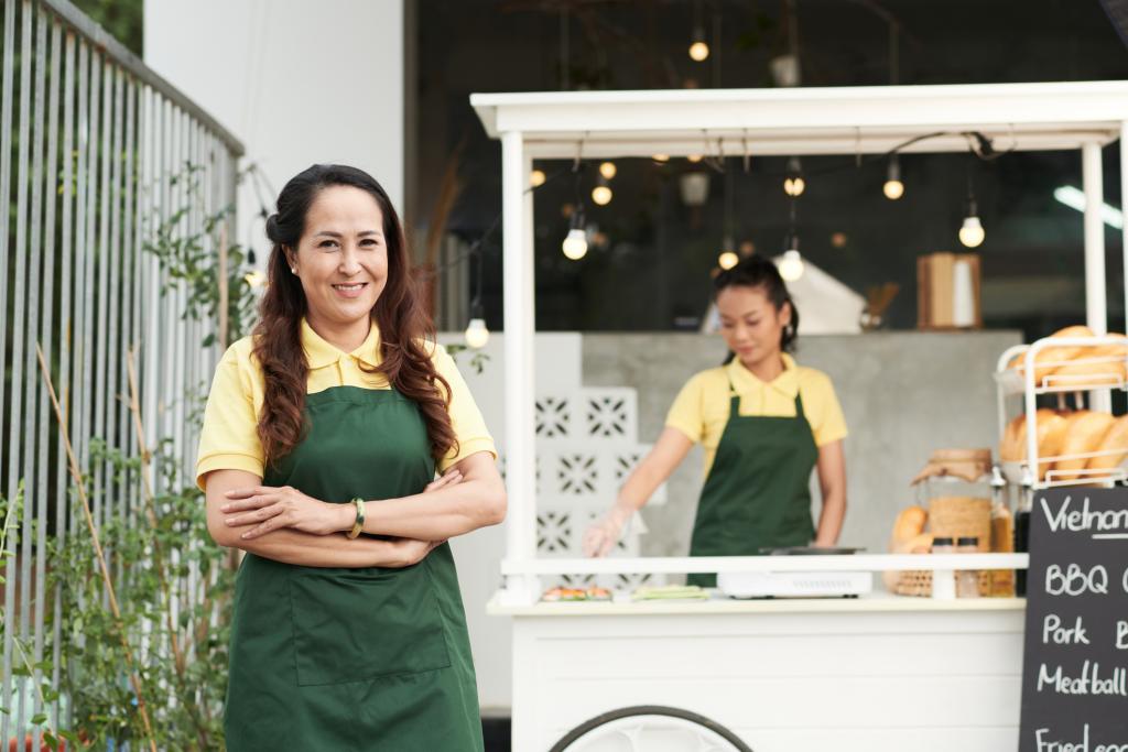 Food cart owner standing and smiling in front of their stand