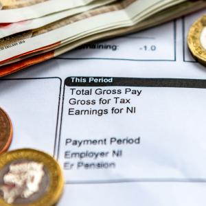 A payslip showing pay as you earn tax deductions, national insurance and pension contributions with some bank notes and coins.