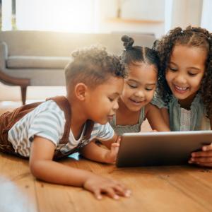 Three siblings watching a tablet together and smiling